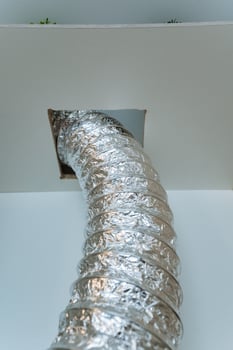 A shiny silver duct is creatively protruding from a small hole in the ceiling above, adding a somewhat intriguing visual element to the otherwise plain and simple structure of the room photo