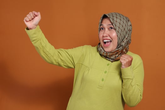 Joyful muslim woman celebrates success with excitement and energy indoors photo