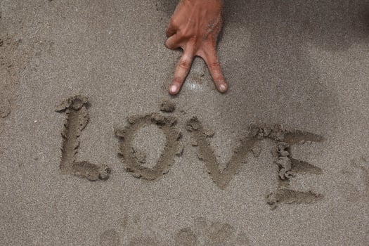 Love Message Written on Sand with Hand Gesture showing peace sign, summer season photo