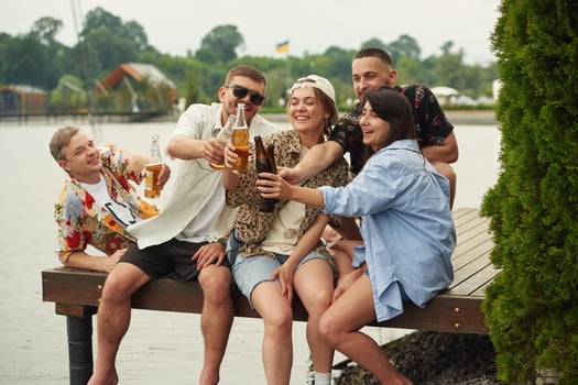 Celebrating,, having fun. Group of friends are sitting near the lake with beer in hands photo