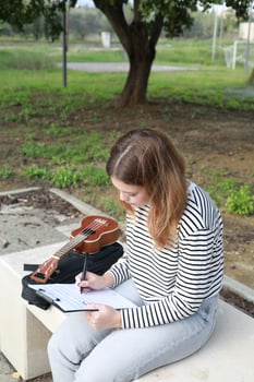 Girl Writes Notes On A Sheet Music To Play Them With The Ukulele Vertical View photo