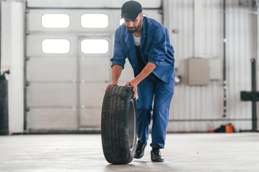 Walking with new tire. ..Auto mechanic, working in garage. Repair service photo