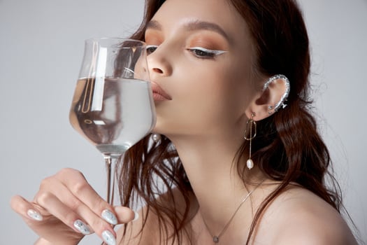 Young adult woman holds glass of water in her hand near face. Beautiful makeup, clean skin photo