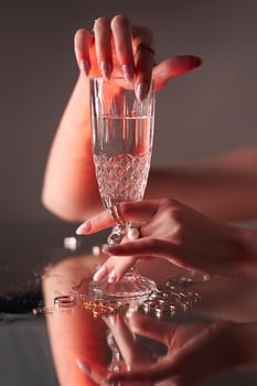 Woman holds glass glass in her beauty hand. Rings and jewelry on table, luxurious life. Alcoholism photo