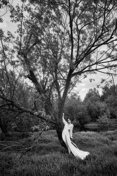 Erotic young woman in a long white dress walks in a spring park near river. Sexy brunette posing in nature 4 photo