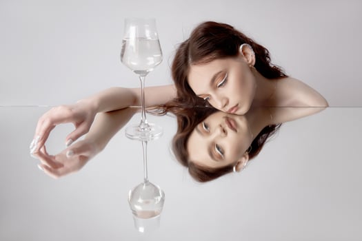 Reflection of woman in mirror with glass in her hand. Beautiful face makeup, natural cosmetics photo