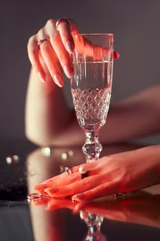 Woman holds a glass glass in her beauty hand. Rings and jewelry on table, luxurious life. Alcoholism. photo