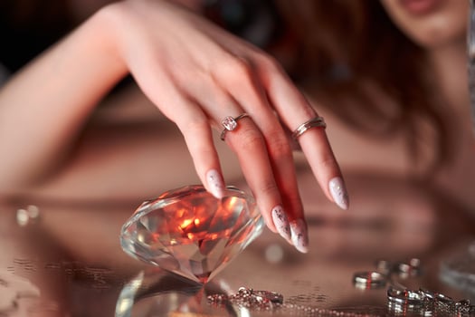 Beauty Woman holds big diamond in hand while lying on table. Beautiful hands, professional manicure, large brilliant. photo