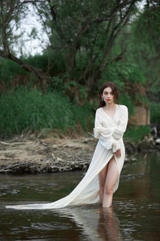 Erotic young woman in a long white dress walks in a spring park near river. Sexy brunette posing in nature 3 photo