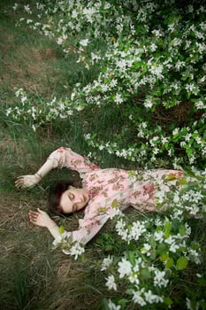 Beautiful young woman lies in grass under blooming apple tree Romantic girl is resting in nature. Spring portrait of woman photo