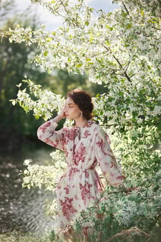 Beautiful romantic woman stands in branches blooming apple tree. Spring portrait girl in flowers apple tree photo