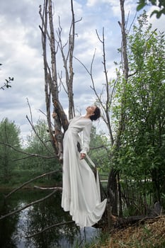 Fantastic fairy beautiful woman in white long dress on old dry tree Girl princess in swamp. Fashion model sexy girl posing on a tree on lake. Fairy tale photo