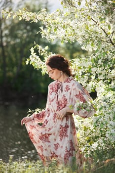 Beautiful romantic woman stands in branches of blooming apple tree. Spring portrait girl in flowers apple tree.. photo