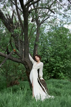 Erotic young woman in a long white dress walks in a spring park near river. Sexy brunette posing in nature.. photo