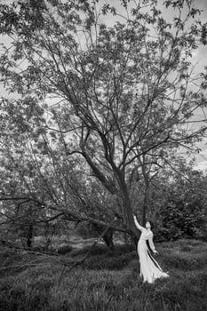 Erotic young woman in a long white dress walks in a spring park near river. Sexy brunette posing in nature. photo