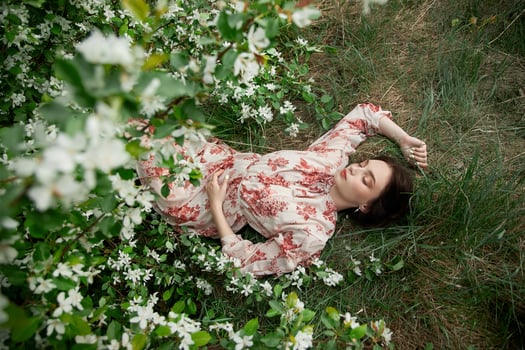Beautiful young woman lies in grass under blooming apple tree. Romantic girl is resting in nature. Spring portrait of woman. photo