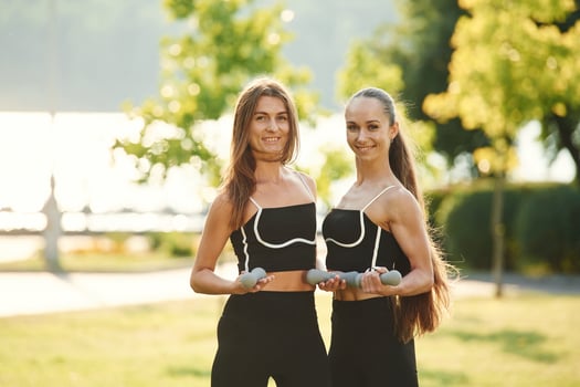 With dumbbells. Two women in sport clothes are doing exercises outdoors on the field photo
