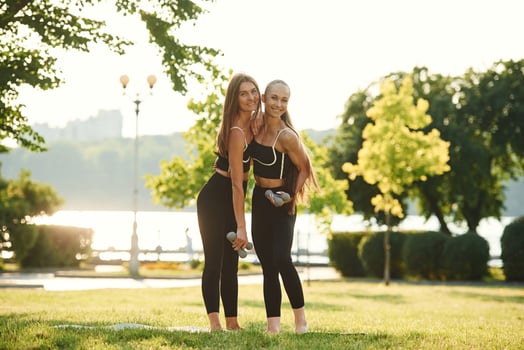 Dumbbells ,in hands. Two women i,n ,sport clothes are doing exercises outdoors on the field photo