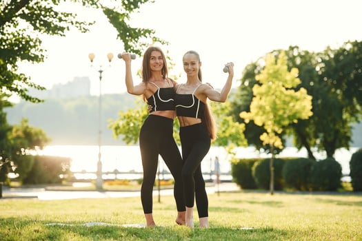 Dumbbells in ,hands. Two ,wome,n in sport clothes are doing exercises outdoors on the field photo