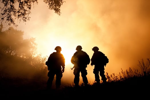 Three men in military gear stand in front of a sunset photo