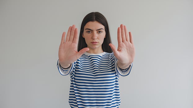 Young woman shows stop gesture serious expression blue striped shirt neutral background simple image photo