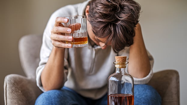 Person struggling with alcohol addiction holding a glass of whiskey feeling hopeless and alone in photo