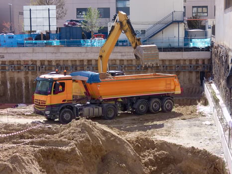 Construction site with orange dump truck and excavator digging at urban location during daylight hours photo