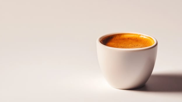 Small white cup with dark brown coffee. Liquid inside the cup is creamy. Coffee cup on a bright plain surface. Light and shadow detail. photo
