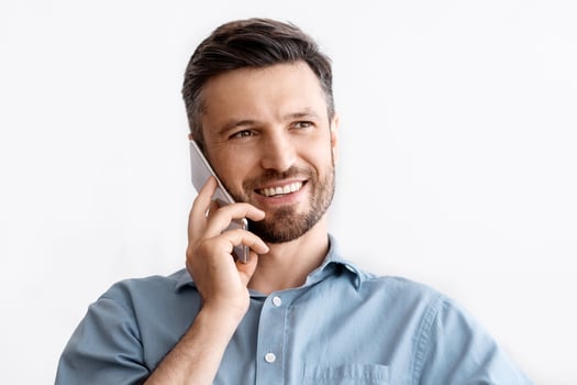 Business Communication. Successful Businessman Sitting At Workplace Talking On Mobile Phone With Client, Having Pleasant Conversation, Sitting At Desk In Office, Smiling And Looking Away, Free Space photo