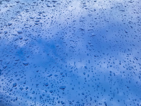 Raindrops and reflections on the blue metal surface of the hood on a summer day. photo