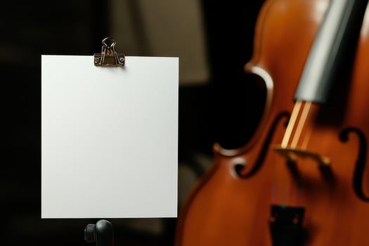 A white clipboard with a blank piece of paper is on a stand next to a cello photo