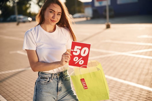 Minus fifty percent sale. Half the price. .Beautiful woman in casual clothes is holding shopping bags, outdoors photo