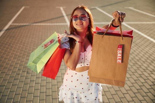 Showing, shopping bag with sale stickers on it. Beautiful woman in casual clothes is outdoors photo