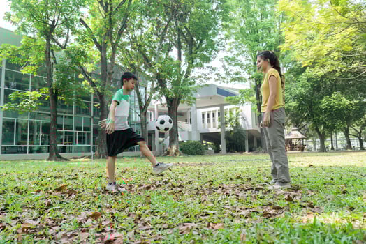 Skill Development and Family Togetherness. A young boy showcases his impressive soccer skills while his mother cheers him on. photo