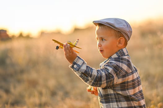 In the soft golden hour glow, a boy in suspenders and a cap plays joyfully with a bright yellow metal airplane. photo