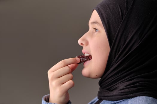 A profile portrait of Muslim girl with hijab eating a dates isolated on black background studio. photo