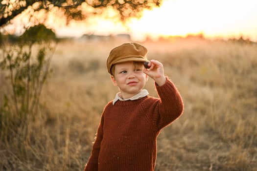 Captured in a sepia-toned style, a boy with a classic newsboy cap carefully observes an olive in his hand, reflecting the charm of a bygone era. photo