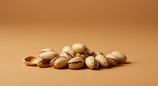 A heap of pistachios with open shells displays their vibrant green kernels on a warm surface. photo