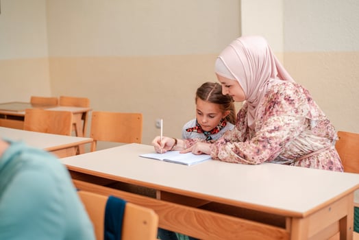 Female hijab Muslim teacher helps school kid to finish the lesson during the class in the classroom. photo