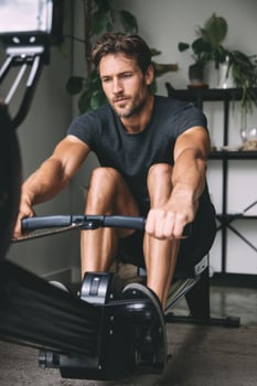 Rowing workout session with a focused man exercising indoors, showcasing strength and determination in a modern fitness environment, fitness lifestyle concept photo