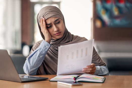 Frustrated muslim woman in hijab financial manager working while sitting at cafe, using laptop and checking documents, copy space. Upset arab lady looking at papers, having difficulties with job photo