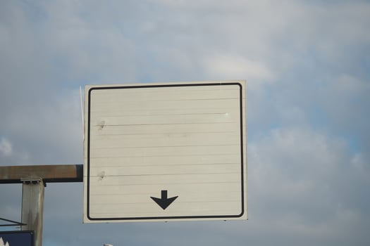 Blank traffic sign points downward amidst a cloudy sky photo