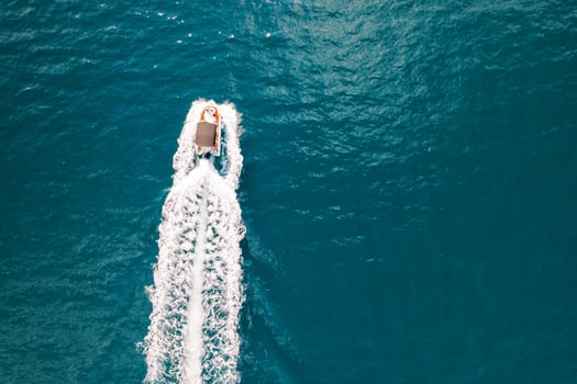 Motorboat sails on a turquoise sea, leaving behind a white foamy trail. Top view photo