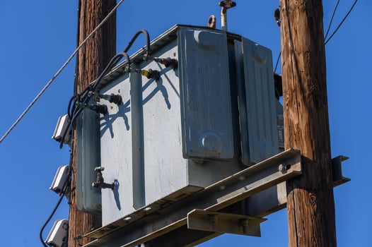 Power transformer mounted on utility pole under bright blue sky during midday in a suburban neighborhood photo