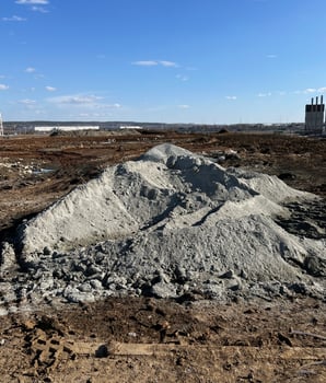 Large pile of gravel at a construction site under a clear blue sky. Industrial area in the background with construction materials scattered on the ground, active work zone photo
