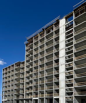 High-rise building under construction with exposed concrete framework and wooden scaffolding under a clear blue sky background, modern urban development progress photo