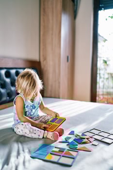 Little girl collects a puzzle on the tablet on the bed photo