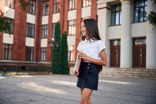 Front view. ,School girl in uniform is outdoors near the building photo