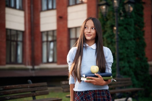 An apple, on the books. School girl in uniform is outdoors near the building photo