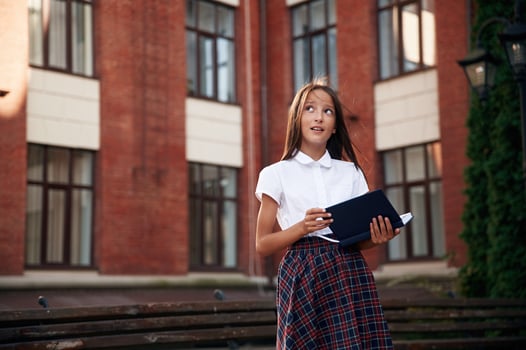 Thinking,, thoughtful look. School girl in uniform is outdoors near the building photo